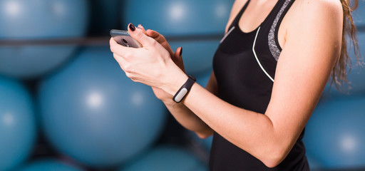 Close-up of female hands with fitness tracker and smartphone in gym