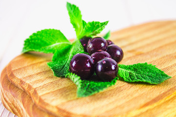 Black currant on a blackboard with a straw and smoothies on a white wooden table.