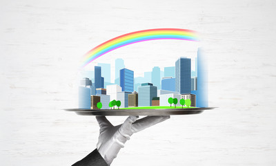 Hand holding metal tray with modern city model against wooden background