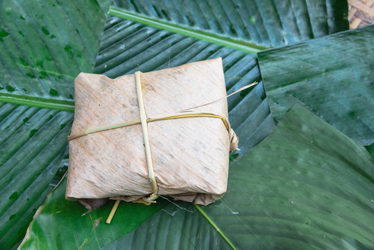 Close-up one traditional cake from the North of Vietnam wrapped on dried banana leaves tie with rice straw on large green leaves called la dong (Phrynium placentarium). Sweet rice cakes (banh gai).