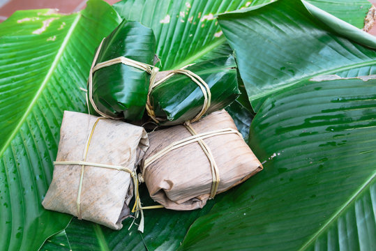 Close-up group of traditional cakes (banh gai) from the North of Vietnam wrapped on fresh and dried banana leaves tie with rice straw on large green leaves called la dong (Phrynium placentarium).