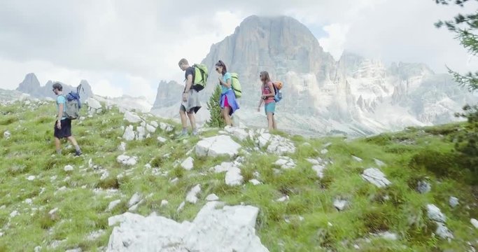 Aerial flight above people hiking along trail path in sunny day. Group of friends summer adventure journey in mountain nature outdoors. Travel exploring Alps, Dolomites, Italy. 4k drone forward video