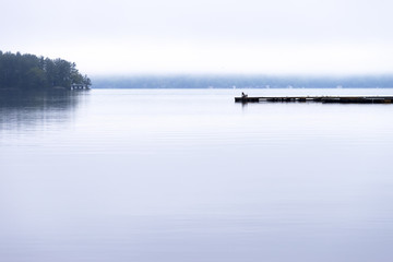 Long pier with adirondack chair silhouetted against a moody landscape obscured by fog