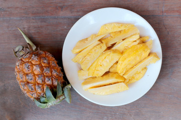 Cutting fresh pineapple and pineapple shelled Asian-style in white dish on the old wooden background. Tropical fruit concept.