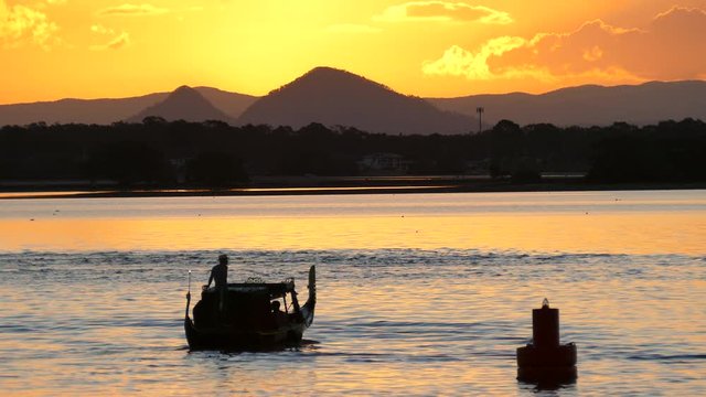 Silhouette of a gondola boat passing by a sunset over mountains.