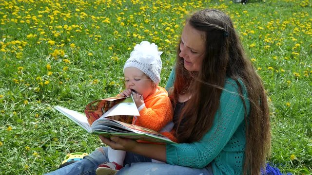 Happy child in a spring glade in dandelions with his family. Sits at the mother's lap and reads a book.