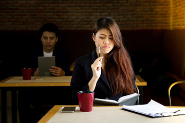Asian businesswoman writing in notebook, while working in a cafe.