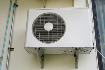 Air conditioner condenser unit at a  white concrete wall