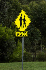 Yellow and black metal road sign warning that aged pedestrians are in area