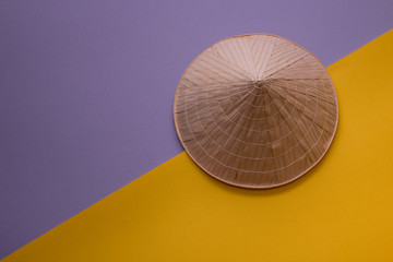 Summer background: Close-up of Asian conic straw hat on purple and yellow. Top view.