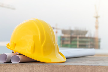 The yellow safety helmet put on the blueprint at construction site with crane background