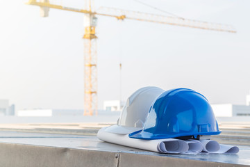 The safety helmet put on the blueprint at construction site with crane background