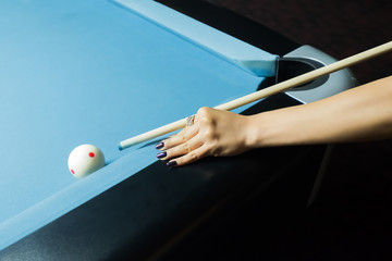 A lady's hand putting on the pool table, aiming on the white ball