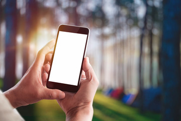 Tourist holding mobile phone take a shot of  touristic tents in forest. Blank screen mobile phone for graphic display montage.