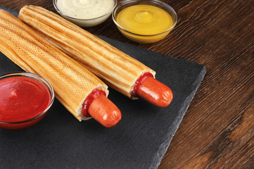 French hot dog and bowls with sauces on a slate board. Fast food.