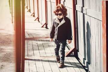 Trendy little boy walking on wooden pathway on a sunny day