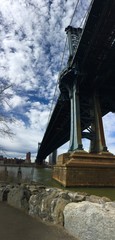 Fototapeta premium Manhattan bridge over the river and rocks at Brooklyn bridge park with cloudy sky