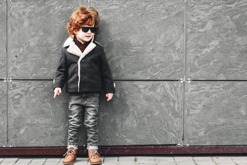 Portrait of a cute trendy boy wearing sunglasses, looking away on the gray background