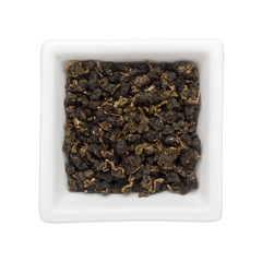 Oolong tea leaves in a square bowl isolated on white background