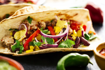 Beautiful tasty appetizing traditional mexican food tacos with meat and vegetables on black slate. Closeup.