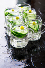 Fototapeta na wymiar Cucumber water in six little mason glass jar on black background.