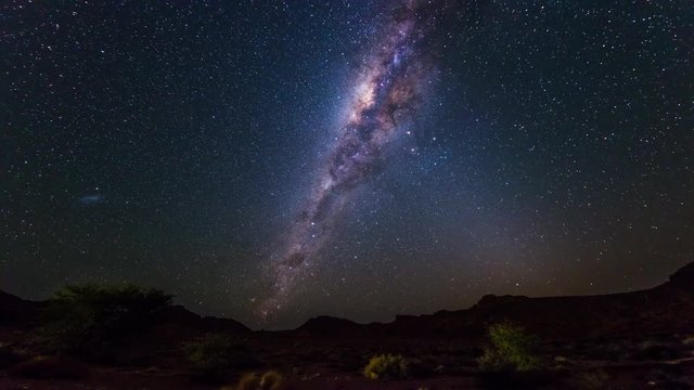 The apparent rotation of an outstandingly bright Milky Way and starry sky beyond the mountains of the Namib desert, Namibia. Time Lapse.