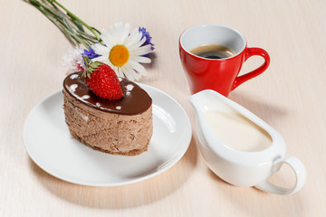 Chocolate cake on the white plate with chamomile and cornflowers, a cup of coffee and a gravy boat with cream
