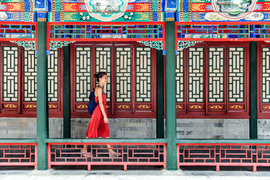 Young backpacker woman walking through old traditional long corridor at chinese temple, china summer travel. Asian girl visiting tourist attraction in Beijing.