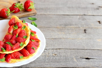 Sweet strawberry omelette. Colorful omelette stuffed with fresh strawberries and garnished with mint on a plate and wooden background with empty place for text. Summer breakfast or lunch idea