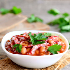 Smoked sausage and white bean stew. Simple white bean stew with smoked sausage, tomato sauce and fresh parsley in a bowl and on a wooden old table. Homemade nutritious stew. Closeup
