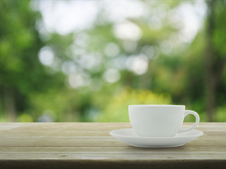 White coffee cup on wooden table over blur green tree in garden