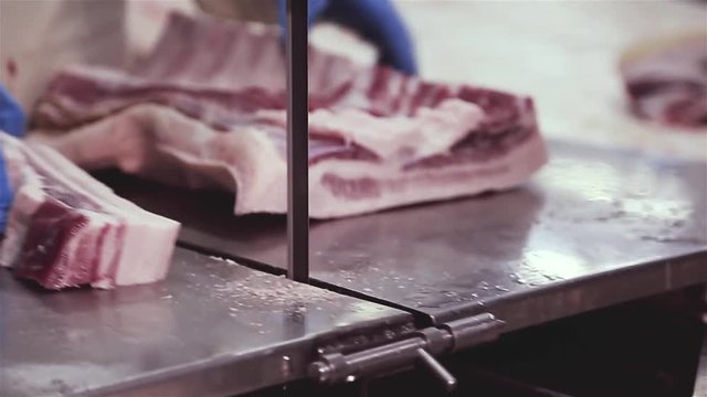Machine for cutting meat with a vertical blade of a saw. The process of cutting carcasses of cattle by means of an automated saw. Manual feeding of meat into a meat grinder. Meat processing plant.