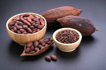 Chocolate bar and dried cocoa pod, cocoa nibs in wooden bowl on black background