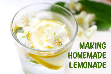 Glass of cold refreshing summer drink with flowers and slices of lemon on table close up