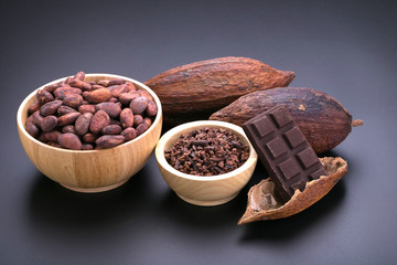 Chocolate bar and dried cocoa pod, cocoa nibs in wooden bowl on black background