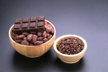 Chocolate bar and dried cocoa seed, cocoa nibs in wooden bowl on black background