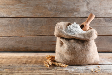 Scoop in sackcloth bag with flour on wooden background