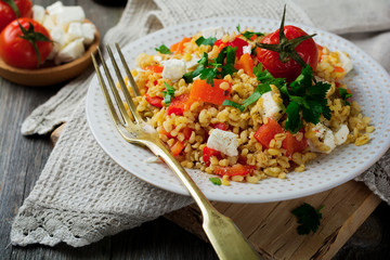 Tabula. Bulgur with baked pepper, tomato and feta cheese on an old wooden background. Selective focus.