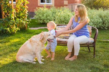 Mother holding baby son and playing with labrador dog in the park