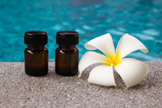 Bottles of aroma essential oil and flower of frangipani on the swimming pool background for spa theme.