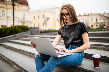 Smiling college student sitting on staircase with laptop in the city