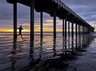 Silhouette of a jogger at sunset under a beach pier 