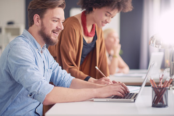 Obraz premium Businessman sitting and using laptop while his colleague standing and helping him