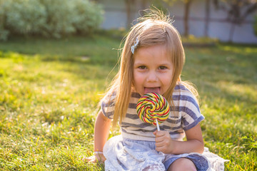 Funny child with candy lollipop, happy little girl eating big sugar lollipop, kid eat sweets