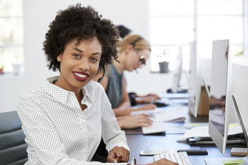 Young black woman with headset smiling to camera in office - obrazy, fototapety, plakaty