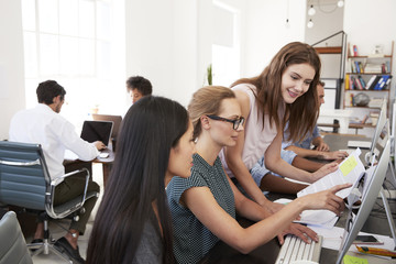 Three women working together at computer in open plan office