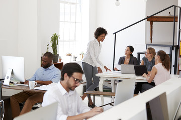 Woman briefing colleagues around a desk in open plan office