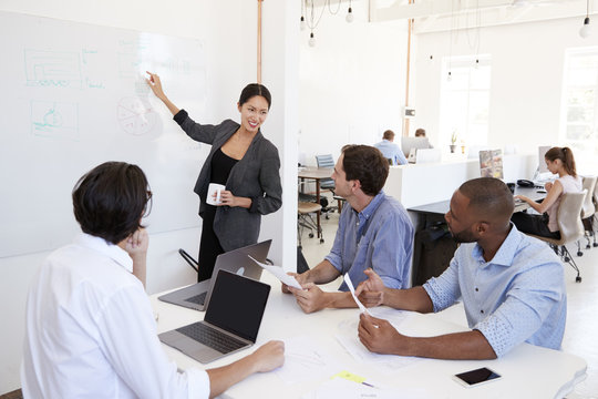 Woman pointing at whiteboard at a meeting in a busy office