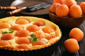 Homemade cheesecake with apricots on black wooden background.