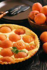 Homemade cheesecake with apricots on black wooden background.